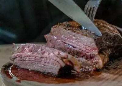 person slicing juicy medium rare meat on top of brown wooden cutting board